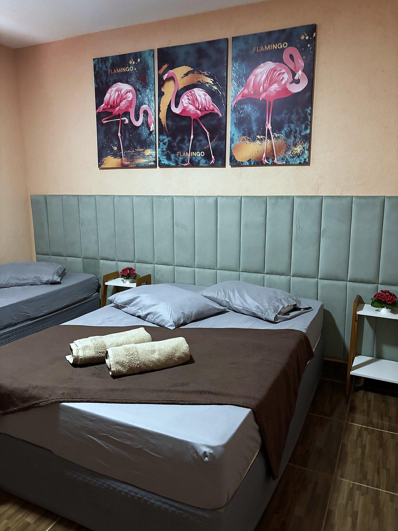 Quarto Flamingo com quadros de flamingos, paredes pêssego e cabeceira em veludo verde-água